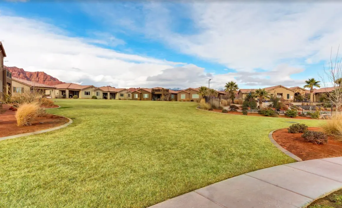 Wide green lawn behind the house, with homes and red cliffs in the distance