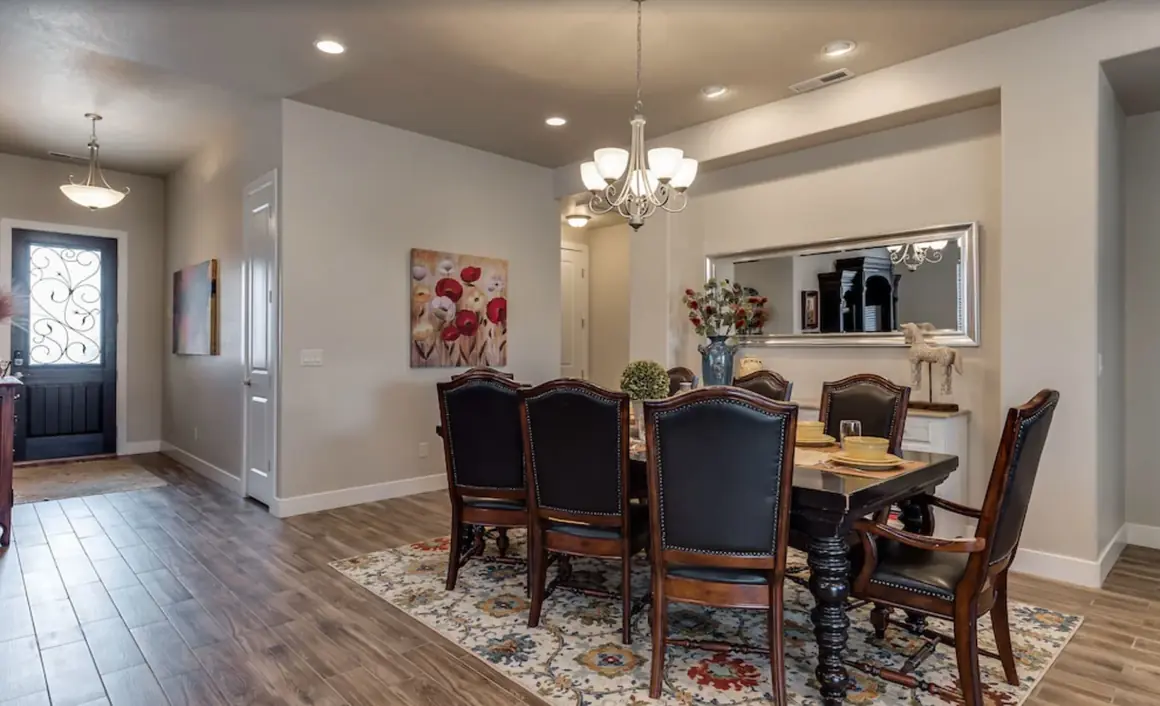 Dining table with leather chairs under a chandelier, front door to the left