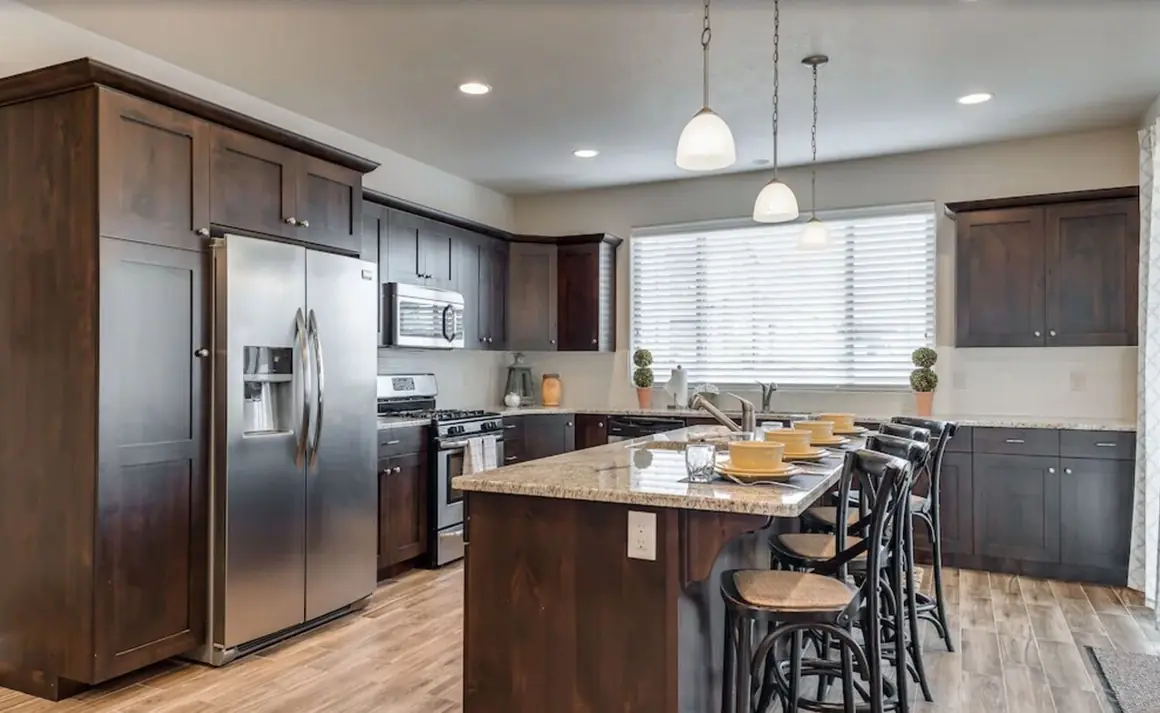 Kitchen with dark wood cabinets, granite island and bar stools, and stainless appliances
