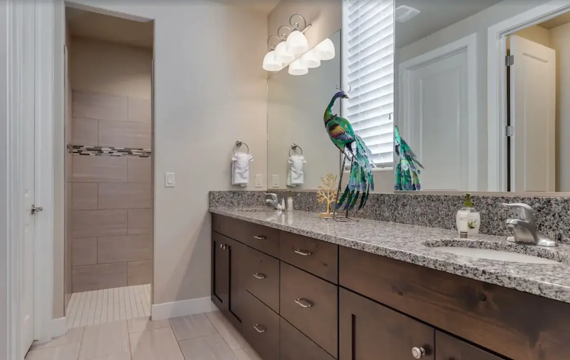 Primary bathroom with a long granite double vanity and tiled shower